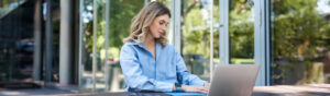 Portrait of beautiful young woman working on fresh air outside. Corporate woman writing in her documents and folders, using laptop outdoors.