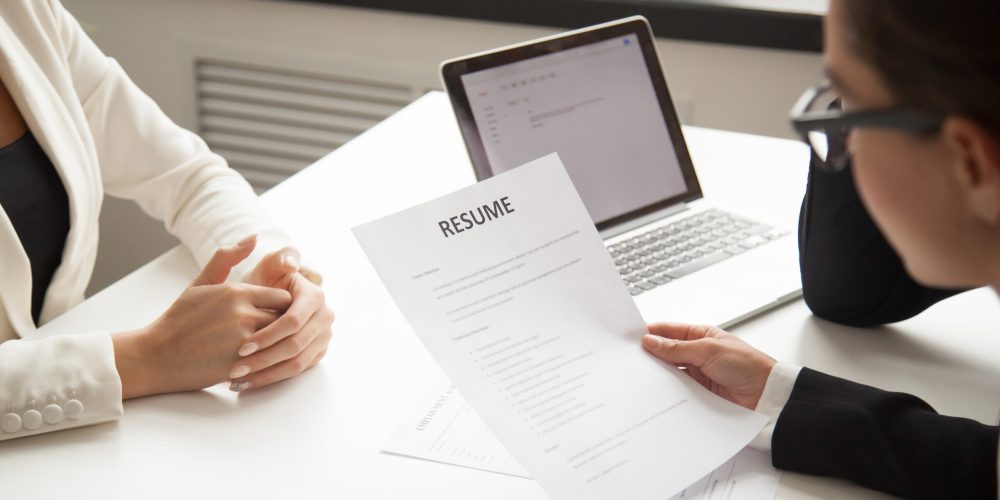 Company CEO and HR manager reading applicant resume or cv while employee waiting for questions, discussion and result during recruitment process in office. Concept of hiring, employment. Close up view