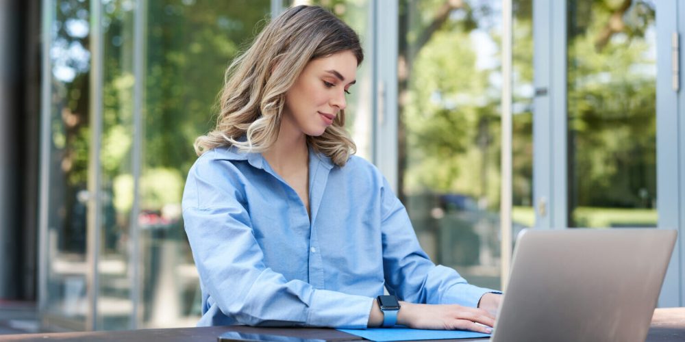 Portrait of beautiful young woman working on fresh air outside. Corporate woman writing in her documents and folders, using laptop outdoors.