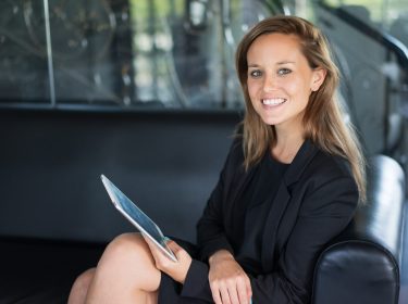 Closeup portrait of smiling young beautiful business woman looking at camera, holding tablet computer and sitting on couch. Technology concept.